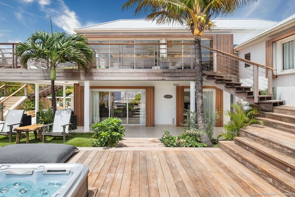 Une maison moderne à deux étages dotée d’une terrasse en bois, d’un espace salon extérieur et d’un jacuzzi.