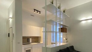 A modern living room with a black sofa, a glass partition, and a kitchen in the background.