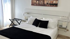 A modern bedroom with a large bed, white headboard, and a cityscape painting above it.