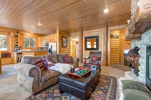 A log cabin interior with a living room, kitchen, and fireplace.