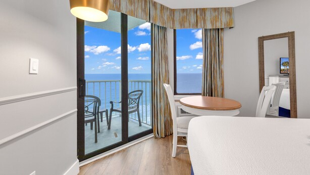A hotel room with a balcony, a dining table, a chair, and a bed. -  Oceanfront Condos At the Strand (Myrtle Beach)