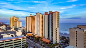 A high-rise hotel with multiple floors, a parking area, and a view of the beach. -  Oceanfront Condos At the Strand (Myrtle Beach)