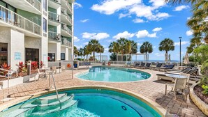 A pool area with lounge chairs, a pool, and a building with balconies. -  Oceanfront Condos At the Strand (Myrtle Beach)