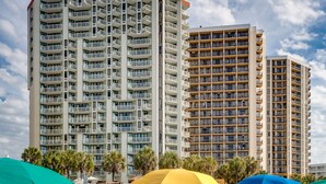 A beachfront hotel with multiple high-rise buildings, beach chairs, and umbrellas. -  Oceanfront Condos At the Strand (Myrtle Beach)
