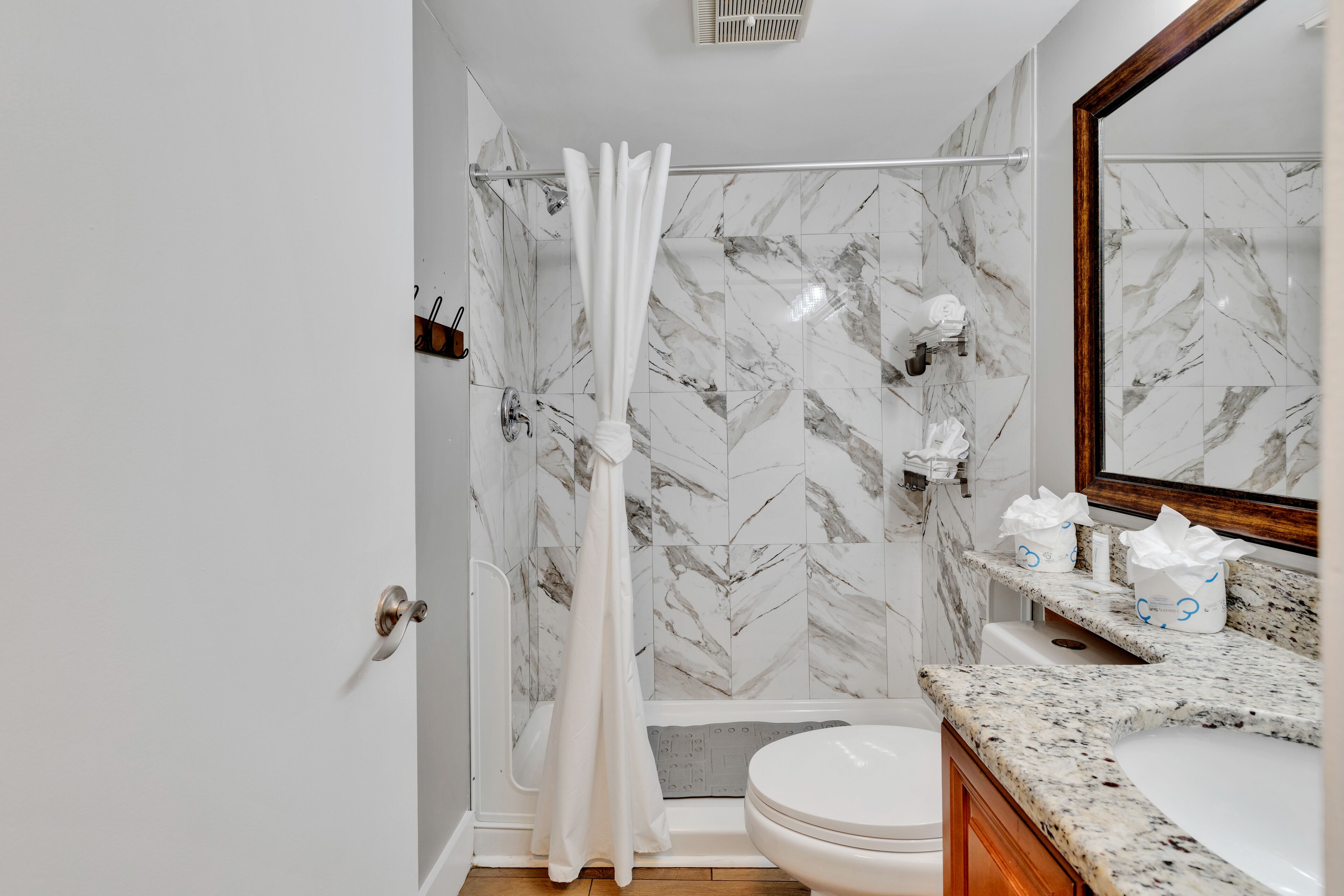 A bathroom with a shower, toilet, and marble-tiled walls.
