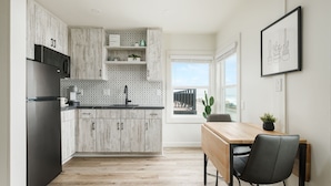 Een moderne keuken met lichte houten keukenkastjes, een zwarte koelkast en een houten eettafel met een stoel.