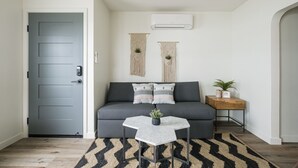 Een moderne woonkamer met een grijze deur, een grijze bank, een klein tafeltje met een plant en een macramé wandversiering.