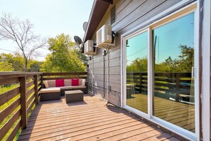 Una terraza con un sofá y cojines, barandilla de madera y un gran ventanal corredero.