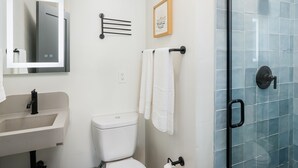 Une salle de bain moderne avec un lavabo blanc, des toilettes, une douche en verre et un porte-serviettes fixé au mur.