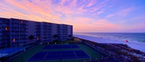 A tennis court with a view of the ocean and a hotel building in the background.