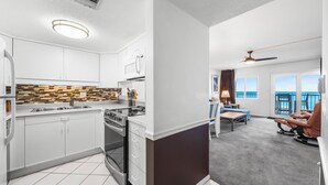 A modern kitchen with white cabinets, a microwave, and a stove. There is a dining area with a table and chairs, and a view of the ocean through large windows.