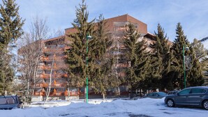 Un edificio de varios pisos con fachada de ladrillo, rodeado de árboles perennes y un estacionamiento cubierto de nieve.