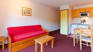 Un espacio habitable pequeño con un sofá rojo, una mesa de centro de madera y una zona de kitchenette.