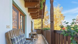 Un espacio de estar al aire libre con techo, bancos de madera y una mesa, rodeado por una valla de madera y plantas.