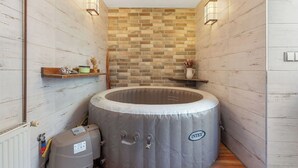 Un baño pequeño con pared de ladrillo, una bañera hidromasaje integrada y estantes de madera con artículos de aseo.