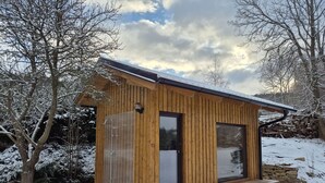 Una cabaña de madera con puerta y ventanas de vidrio, rodeada de árboles cubiertos de nieve.