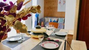 Une table à manger dressée avec des assiettes, des verres et des couverts, et un vase rempli de fleurs séchées au premier plan.