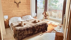 Une chambre à coucher avec une tête de lit en bois, un lit recouvert de draps blancs, un tapis en peau de vache et une décoration murale représentant des bois de cerf.