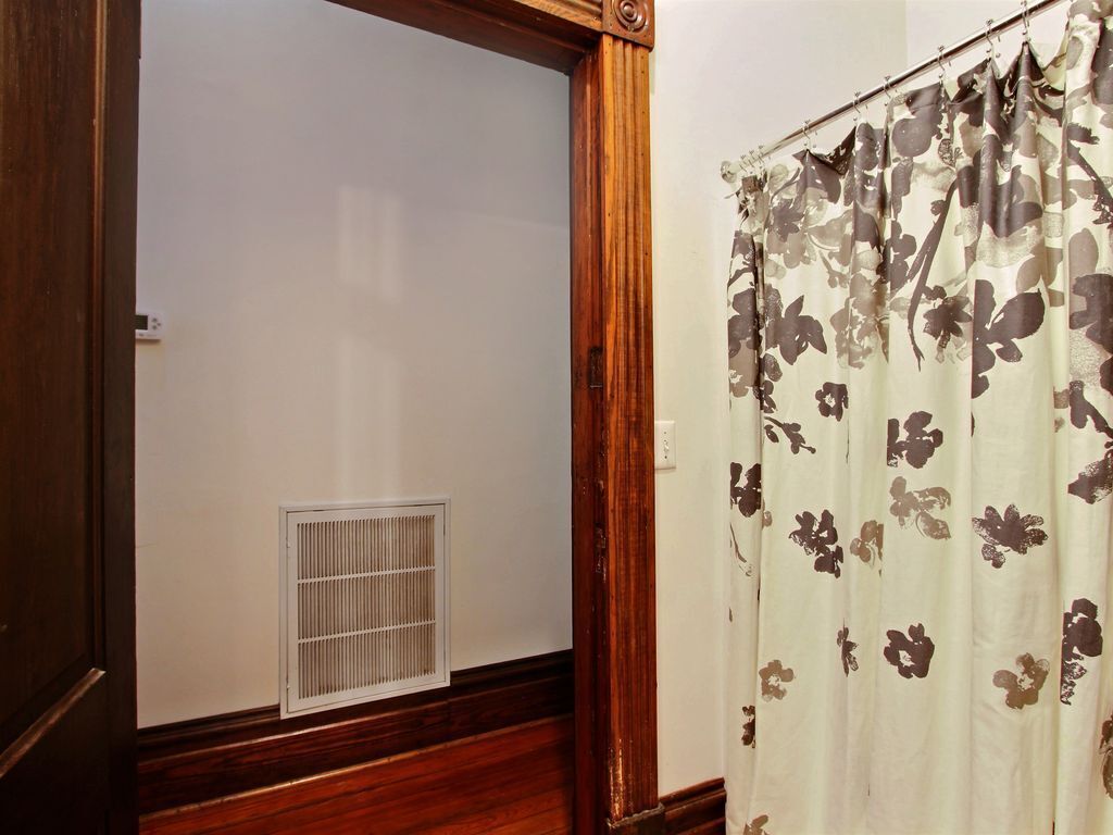 Een kamer met een houten deur, een ventilatie rooster aan de muur en een bloemen gordijn.