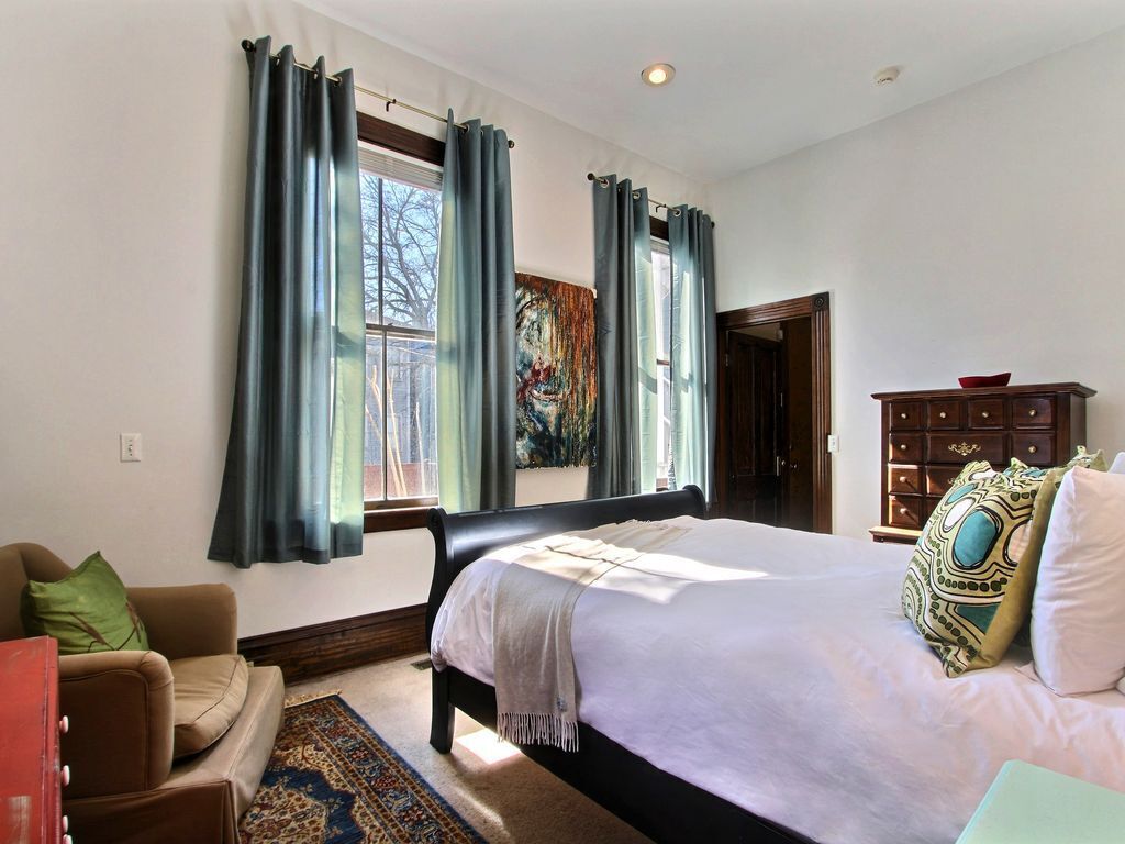Une chambre avec un grand lit, une commode, un canapé et une fenêtre avec des rideaux.