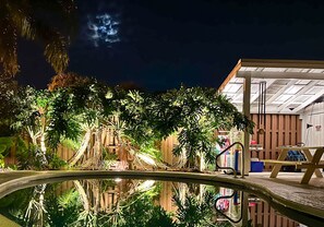 A nighttime view of a pool area with lush greenery and a wooden deck. - LunaSea Beach House - Family friendly, steps to beach, private pool & hot tub (St. Augustine)