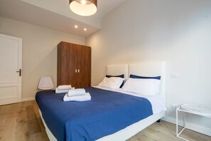 A bedroom with a bed, a wooden wardrobe, a bedside table, and a lamp.