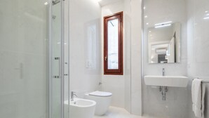 A modern bathroom with a glass shower enclosure, a bidet, a toilet, and a sink with a mirror above it. - Ponte Vecchio White in Florence by Mmega (Firenze)
