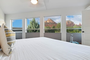 A bedroom with a bed, a window with a view of red rock formations, and a suitcase on the floor.