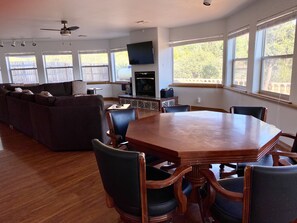 Un salon spacieux avec une grande table à manger en bois, des sièges confortables et un téléviseur à écran plat fixé au mur.