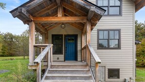 Eine Holzveranda mit einer blauen Tür, einer Treppe und einem kleinen Balkon.