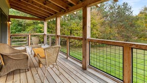 Eine Holzterrasse mit Korbmöbeln und Blick auf eine Rasenfläche und Bäume.