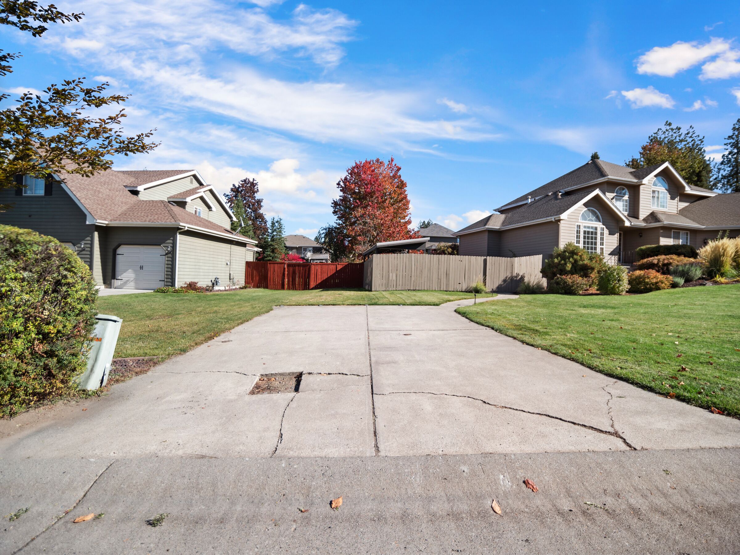 A suburban neighborhood with two houses, a wooden fence, and a driveway leading to a garage.