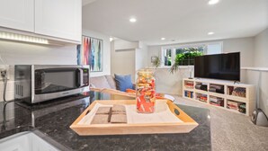 Cozinha moderna com micro-ondas, um suporte com lanches e uma televisão ao fundo.