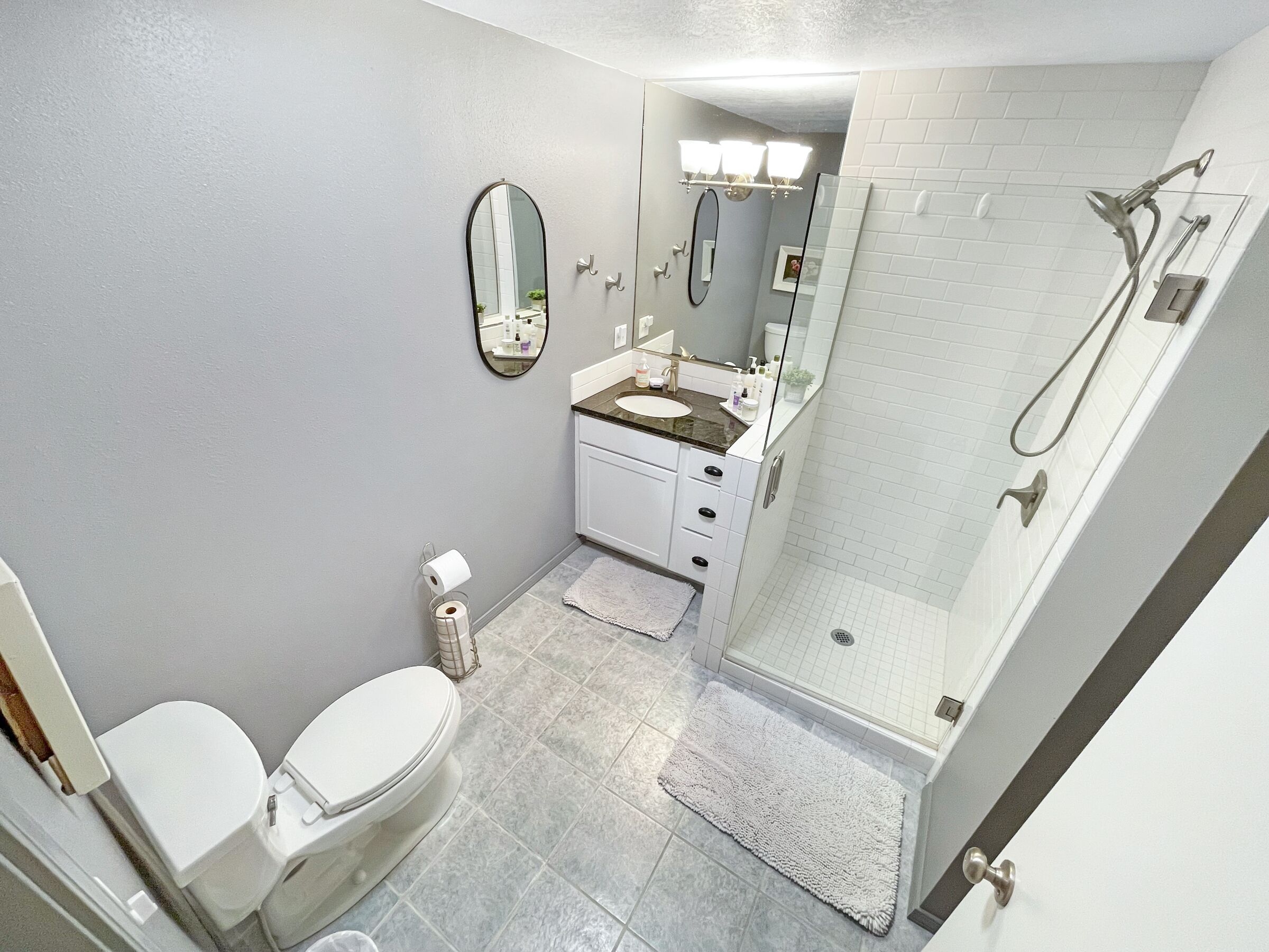 A bathroom with a toilet, sink, mirror, and shower.