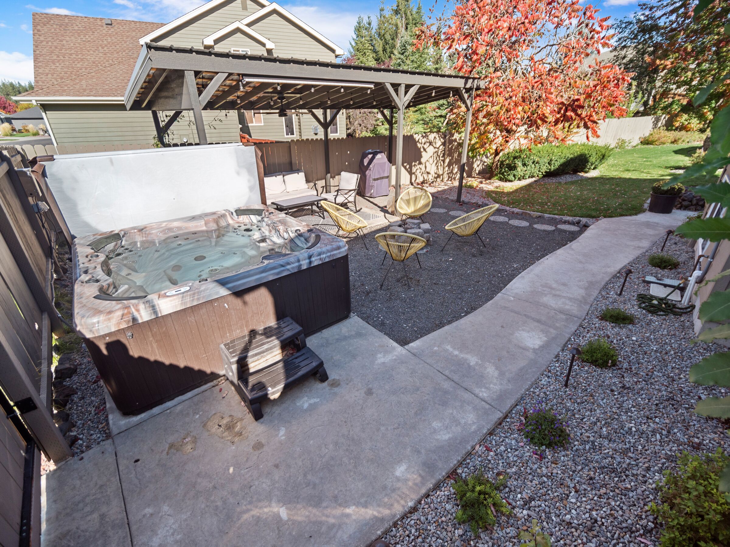 A backyard with a hot tub, outdoor furniture, and a covered patio area.