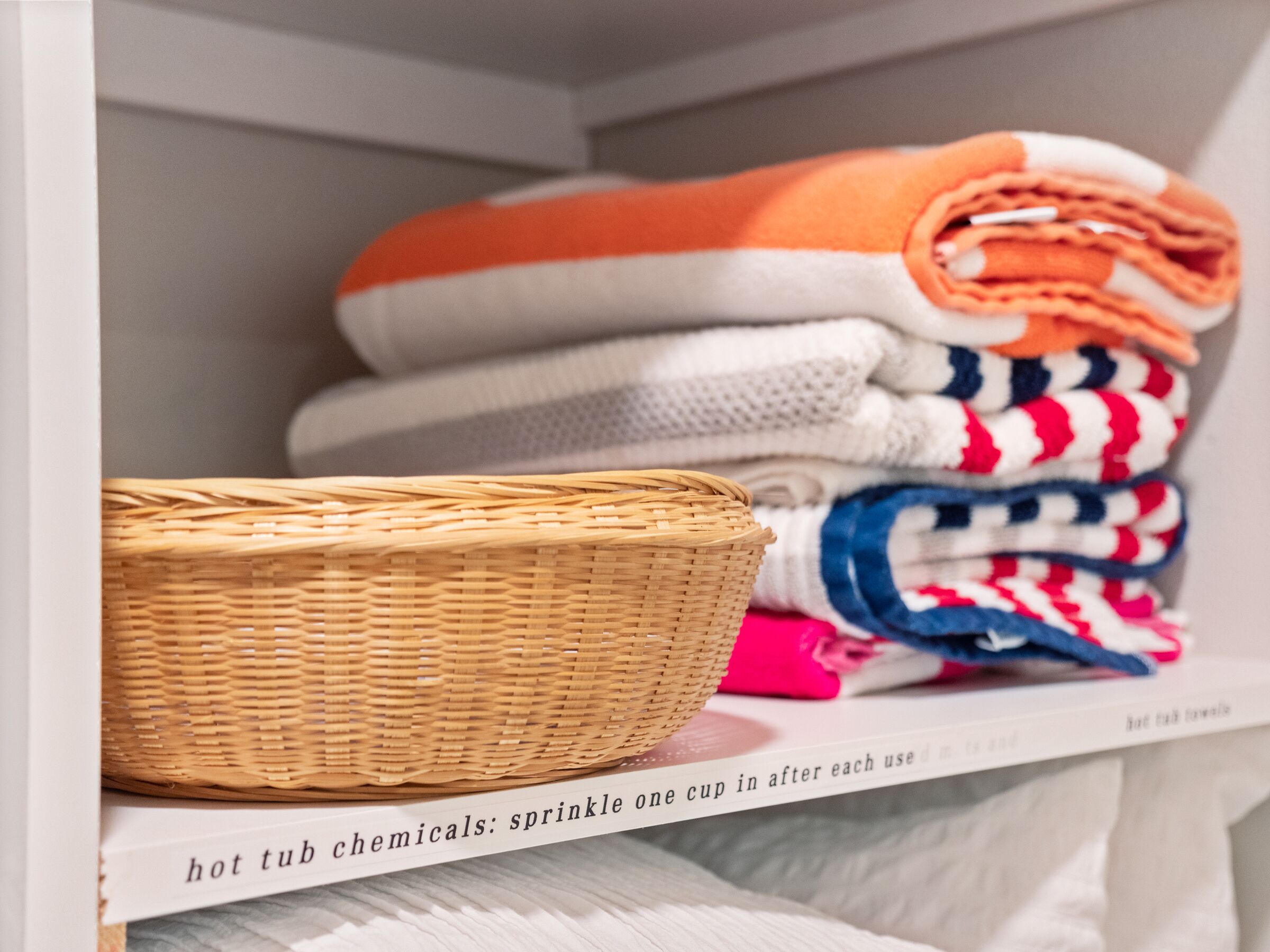 Une étagère avec des serviettes pliées de différentes couleurs et un panier en osier.