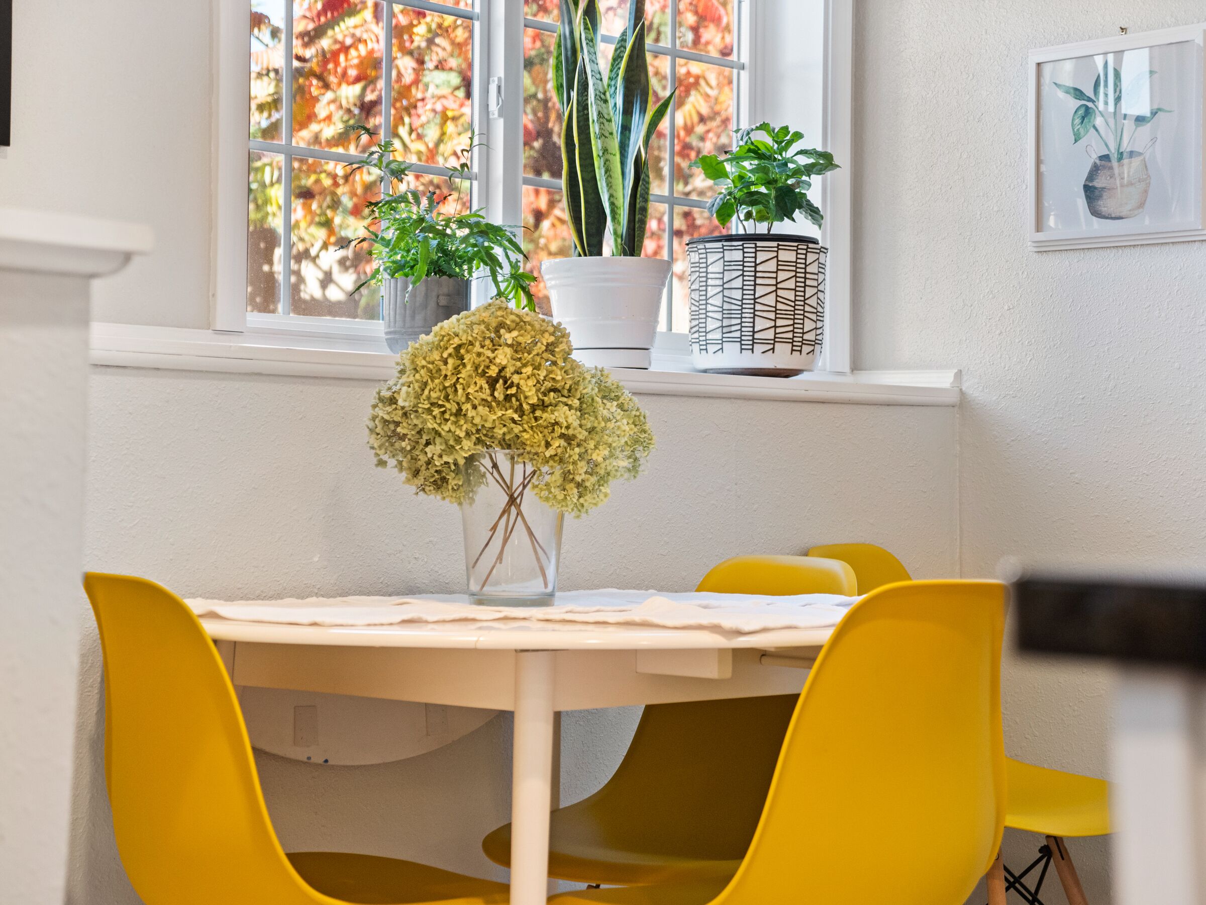 A dining area with a white table, yellow chairs, and a vase of flowers.