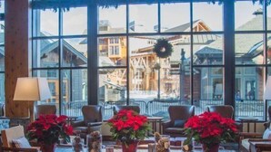A cozy lobby with a leather sofa, a coffee table with red poinsettias, and large windows offering a view of buildings and a wreath on the windowsill. - 1228 Studio at The Lodge at Spruce Peak (Stowe)