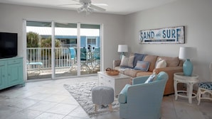 Una sala de estar con un sofá, dos sillones, un televisor y un letrero que dice 'SAND AND SURF'.