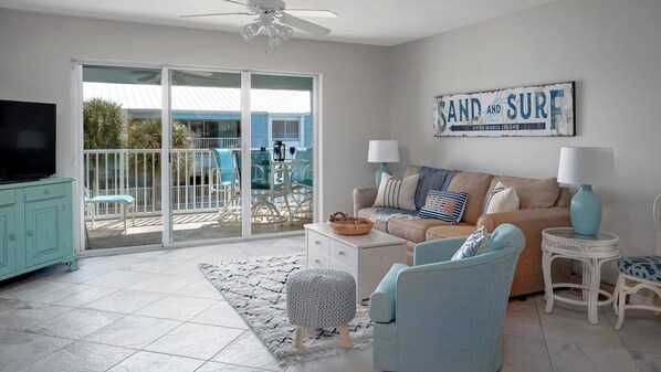 A living room with a sofa, two chairs, a TV, and a sign that reads "SAND AND SURF".