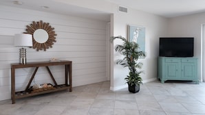 Una sala de estar con una consola de madera, una lámpara, un espejo, una planta en maceta, un televisor y un mueble azul aguamarina.