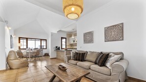 Amplia sala de estar con un sofá color beige, una mesa de centro de madera y un comedor con sillas de mimbre.