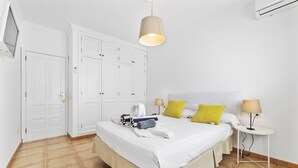 Una habitación de hotel con una cama, dos mesitas de noche, un armario y una lámpara colgante.