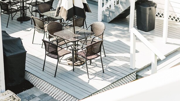 Una terraza con mobiliario exterior, una escalera y una puerta que da a un área cubierta.