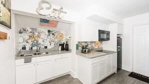 Una cocina moderna con armarios blancos, encimera de granito, microondas y refrigerador.