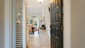 A hallway leading to a dining area with a fireplace, a door with a light fixture, and a patterned rug.