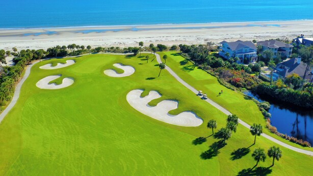 A golf course with sand bunkers, a water body, and beachfront properties.
