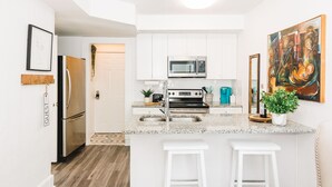 Una cocina moderna con armarios blancos, electrodomésticos de acero inoxidable, una encimera de granito y una zona de bar con taburetes.