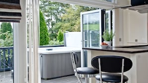 A modern kitchen with a built-in stove, a small bar area with two black chairs, and a view of a garden through large windows. - Watermouth Lodge, Kentisbury Grange (Barnstaple)