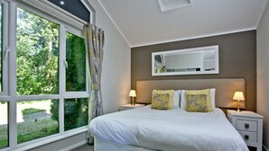 A bedroom with a large window, a bed with two pillows, two bedside tables with lamps, and a mirror on the wall. - Watermouth Lodge, Kentisbury Grange (Barnstaple)